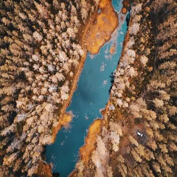 Lac bleu au milieu d'une forêt orangée sur terre ocre.